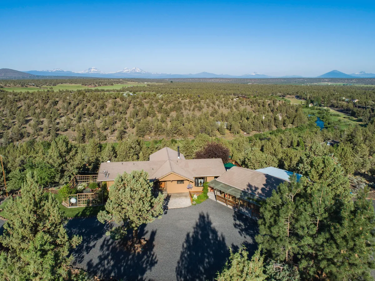 A wide view of the main house amidst open fields, tall trees, and distant mountains, inviting outdoor activities like gatherings, walks, and stargazing. The setting is peaceful, emphasizing the estate's spaciousness and connection to nature.