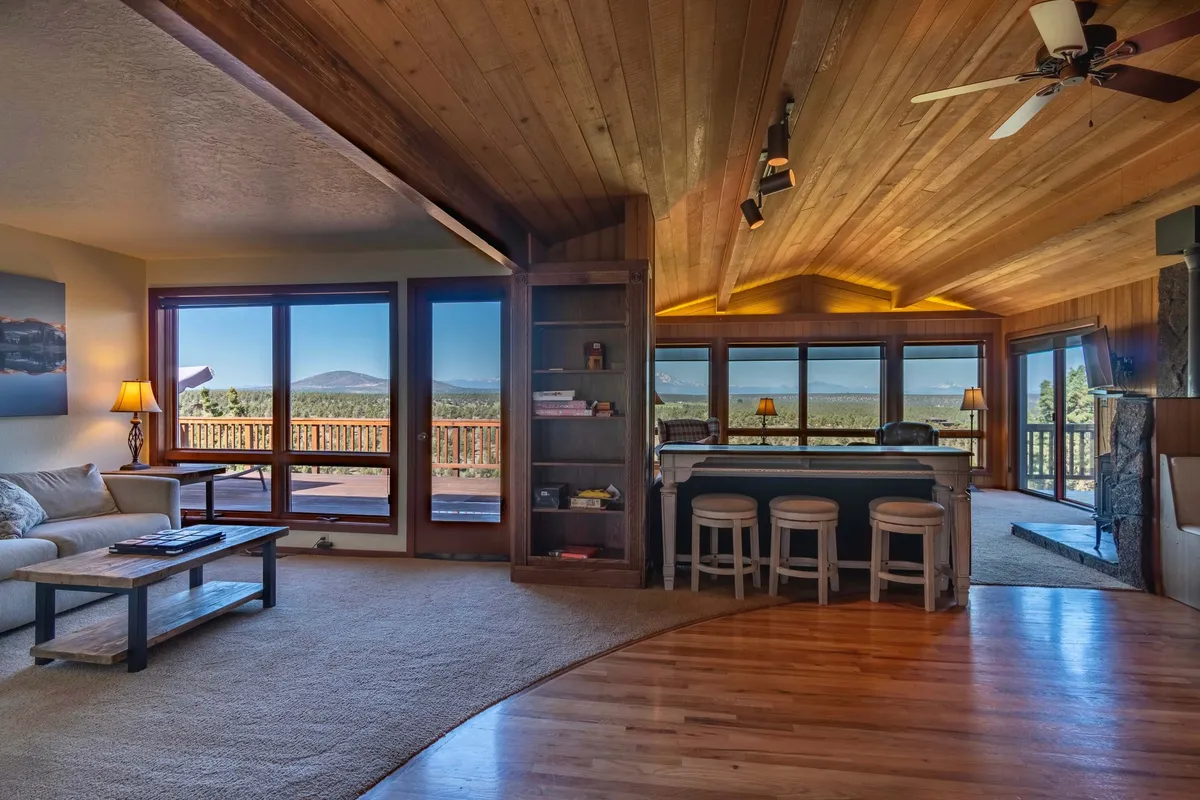 A comfortable seating area with a wooden ceiling, large windows framing mountain views, and a bar with stools set the stage for relaxing or entertaining. The arrangement invites groups to gather, celebrate, or enjoy peaceful moments amidst beautiful surroundings.