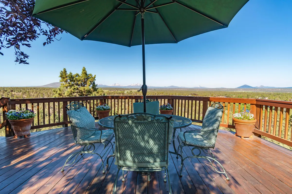 An inviting outdoor dining area set beneath a large green umbrella, with flower pots adding color and charm. The setting opens to a panoramic view of the mountains, making it ideal for al fresco meals while soaking in the landscape.