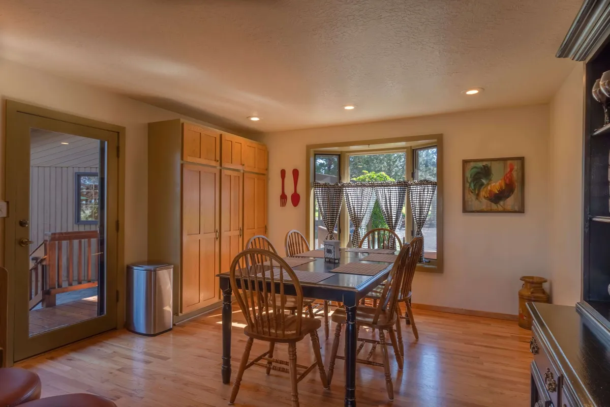 A large dining table sits near a sunny bay window, surrounded by wooden cabinets and cheerful artwork. The setup suggests a welcoming space where groups can gather for shared meals, play games, or celebrate special occasions.