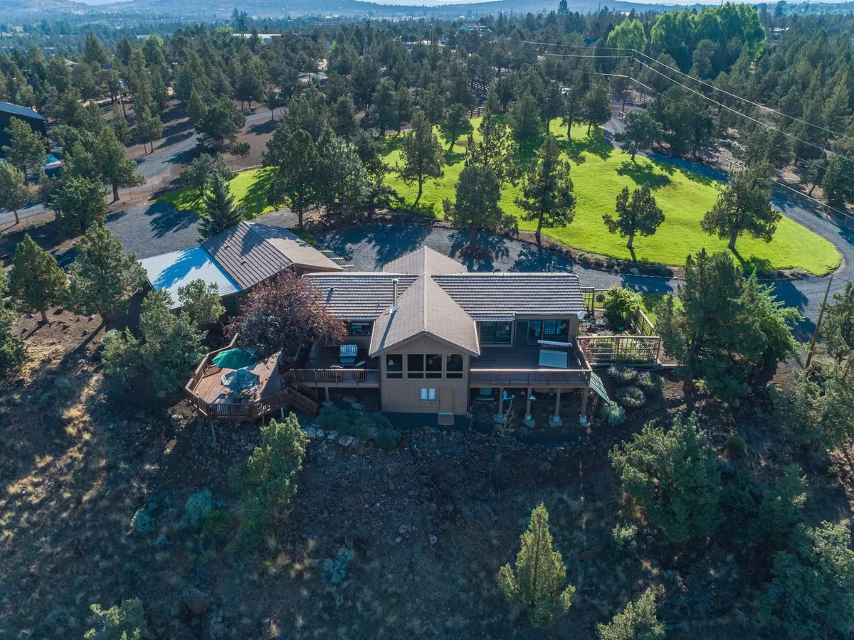 A beautiful lodge-style home perched above the Deschutes River, surrounded by lush greenery and open skies. The expansive deck overlooks scenic mountain views, with inviting spaces for outdoor gatherings and relaxation—including a hot tub perfectly positioned for sunset watching and stargazing.
