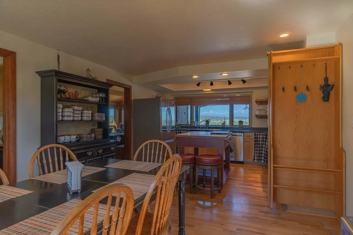 This image showcases the spacious dining area and adjacent kitchen. A large dining table is set for family meals, while the kitchen island provides ample space for group cooking and casual entertaining. A window highlights stunning mountain views, reinforcing the indoor-outdoor connection.