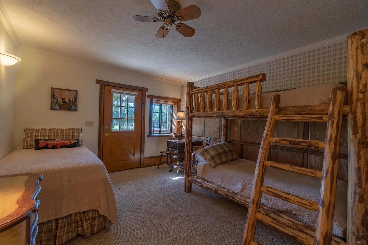This interior shot features a spacious room designed for groups, with multiple bunk beds, a single bed, a wooden desk with a lamp, and warm wood accents. The space is inviting for family gatherings, game nights, and playful downtime, reflecting a lively yet relaxing atmosphere.